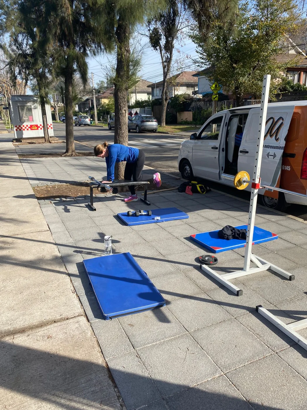 Setup de entrenamiento desplegado en exterior con racks, colchonetas y discos olímpicos